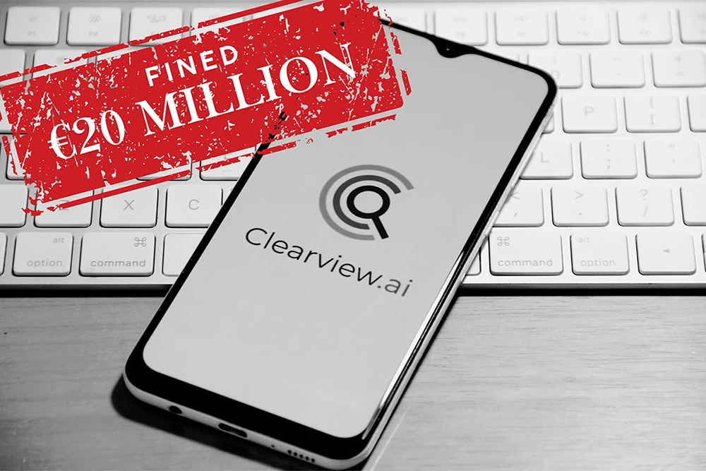 A smartphone displaying the Clearview AI logo on a keyboard, with a red stamp overlay reading "Fined €20 Million," highlighting GDPR penalties for unauthorized facial recognition data collection.