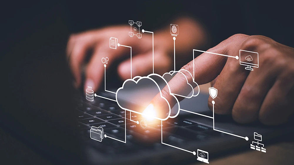 Hands typing on laptop with cloud computing concept overlay.