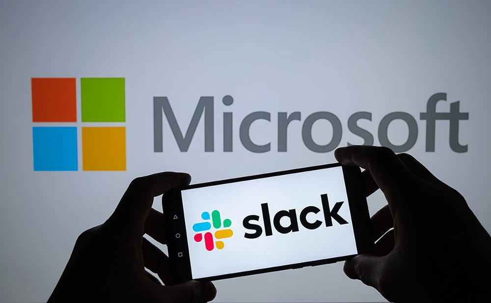 Slack logo seen on smartphone silhouette in hands and Microsoft logo on blurred screen behind. Concept for Slack an antitrust complaint against Microsoft.