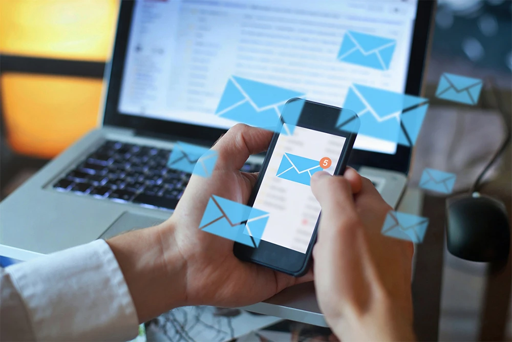 Person checking email support messages on phone with laptop in background.