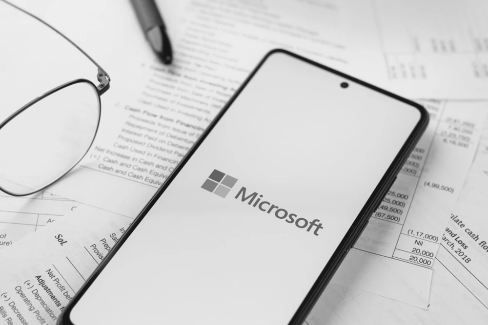 A phone displaying the Microsoft logo on a table full of budgetary documents.