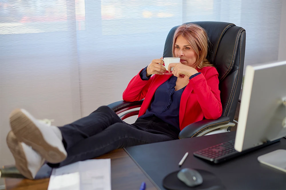 Relaxed professional in red blazer drinking coffee at desk, suggesting confidence in IT support decisions.