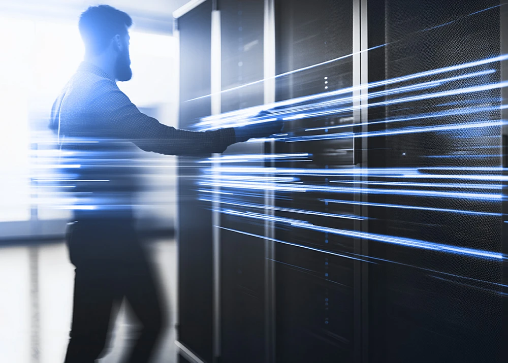 Silhouette of a person in a data center with blue light trails representing data movement.